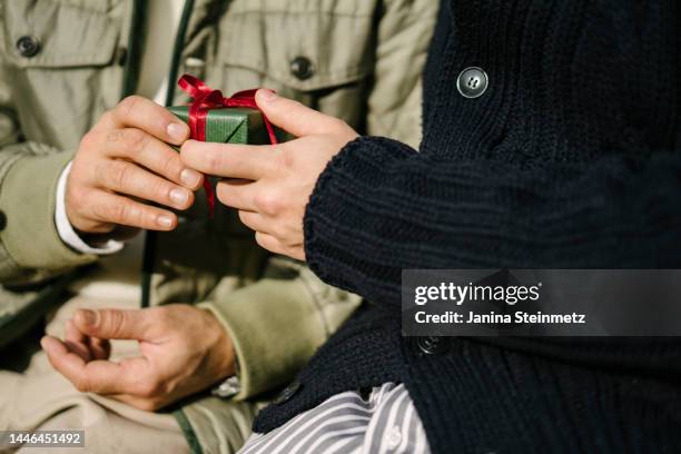 two male hands holding a wrapped surprise gift in their hands - geschenkt stock-fotos und bilder