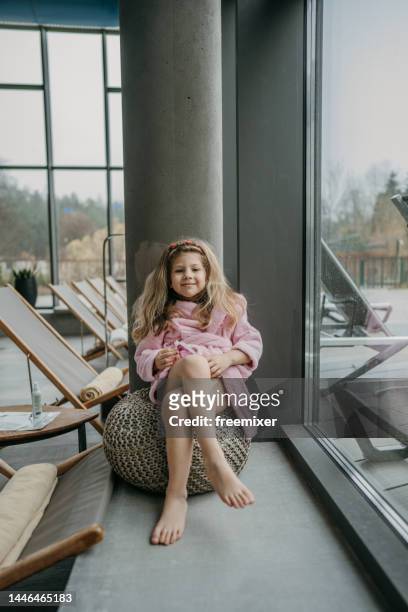 cute little girl in bathrobe sitting by the window on poolside and looking at camera - mini robe stock pictures, royalty-free photos & images