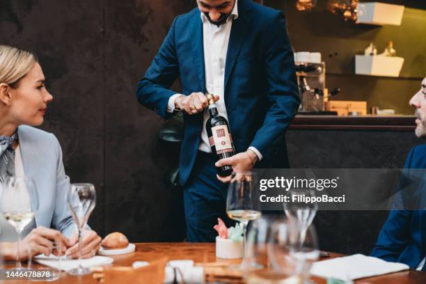 a waiter is serving red wine to clients - sommelier stock pictures, royalty-free photos & images