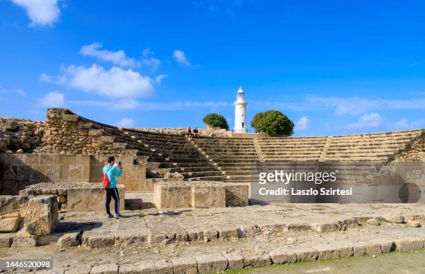 Visitor takes a photo of the Roman Odeon and the Lighthouse at Pafos Archaeological Park on November 22, 2022 in Paphos, Cyprus.