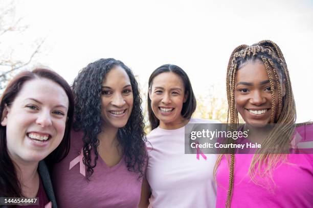 diverse group of women wearing pink ribbons at breast cancer awareness event - social awareness symbol stock pictures, royalty-free photos & images