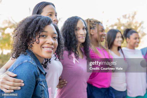 beautiful young adult woman attends breast cancer awareness fundraiser event outdoors with diverse group - mixed race woman stockfoto's en -beelden