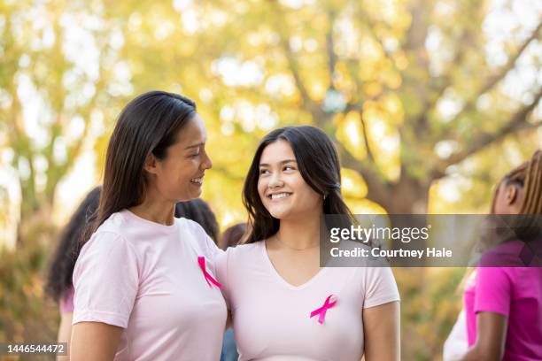 mother and adult daughter wear pink ribbons while attending race to raise money for breast cancer cure - pink october stock pictures, royalty-free photos & images