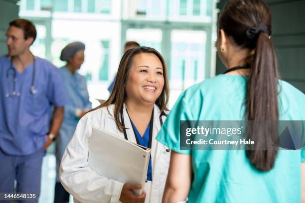 mature adult asian woman is doctor in busy hospital, and is speaking with young nurse about patient care during rounds - busy hospital lobby stockfoto's en -beelden