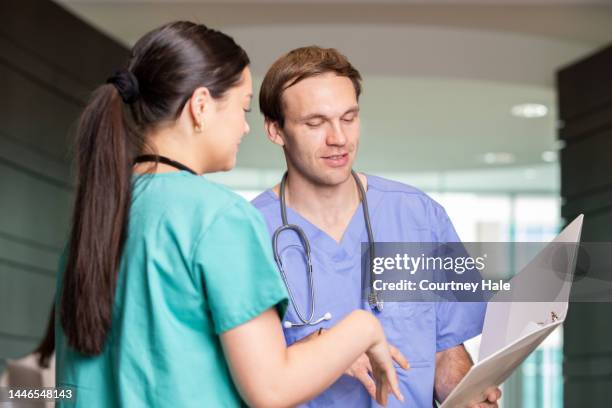 mid adult man is nurse in busy hospital and is speaking with coworker about patient care - busy hospital lobby stock pictures, royalty-free photos & images