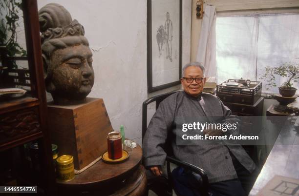 Chinese antique furniture expert Wang Shixiang, seated at his deskin his home in Beijing, China, December 17, 1989. A sculpted head of Buddha sits...