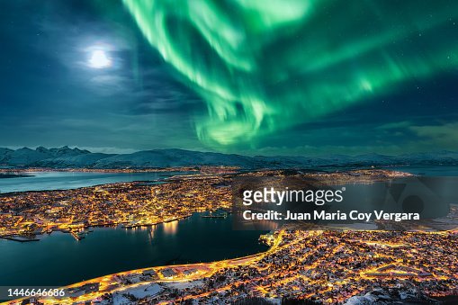 Aurora Borealis dancing over the city of Tromso and full moon, Northern Norway
