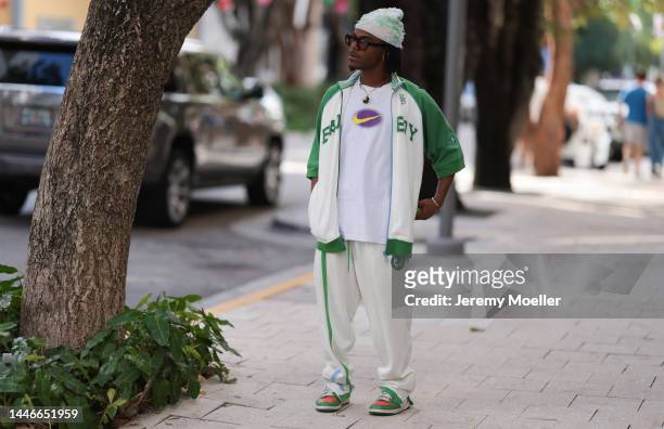 World seen wearing a Nike shirt, a white and green matching jogging suit, dark shades, a hat and sneaker on December 02, 2022 in Miami, Florida.