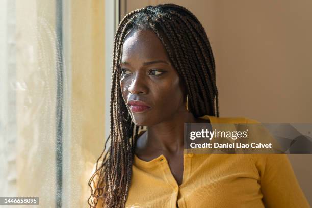 beautiful and pensive 40-year-old woman looking through window - 40 year old black man stock-fotos und bilder