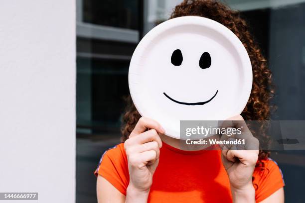 young woman holding smiling emoticon plate over face - smiley face stock-fotos und bilder