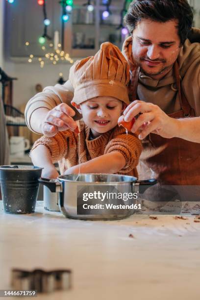 smiling son with father cracking egg in utensil at home - child cooking utensil stock pictures, royalty-free photos & images