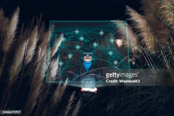 woman amidst plants experimenting immersive experience in metaverse at night - interface dots imagens e fotografias de stock