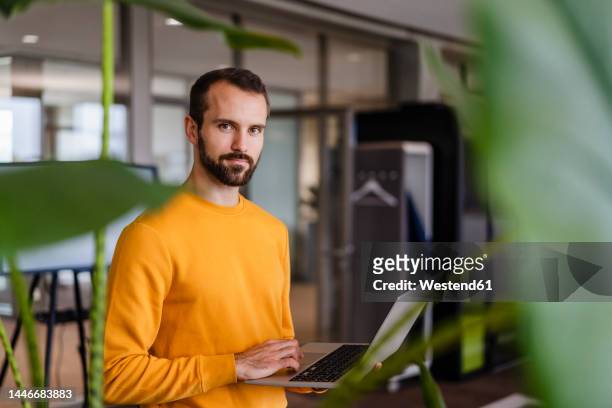 young businessman with laptop in office - blick in die kamera stock-fotos und bilder