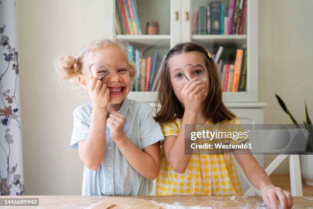 girls looking through heart shaped cookie cutter at home - pastry cutter stockfoto's en -beelden