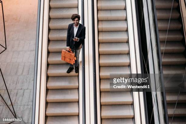smiling businessman moving down from escalator - rolltreppe von oben stock-fotos und bilder