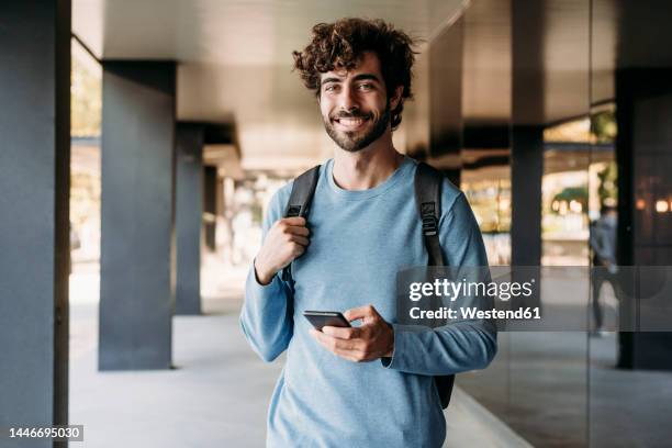 young handsome man with smart phone standing in corridor - young men stock pictures, royalty-free photos & images