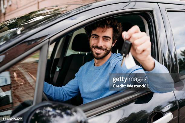 smiling man holding key sitting in car - car key 個照片及圖片檔