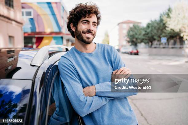 smiling man with arms crossed day dreaming by car - man leaning on car stock-fotos und bilder