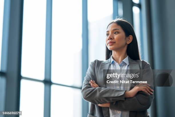 supporting women in business is essential for growth. low-angle view of an asian businesswoman standing with her arms folded and looking away in a modern business office. - インドネシア人 ストックフォトと画像