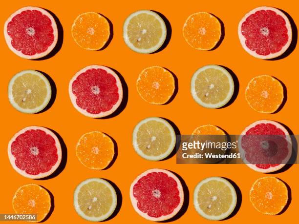pattern of halved lemons, grapefruits and tangerines flat laid against orange background - agrumi foto e immagini stock