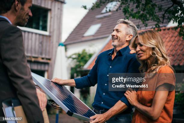 happy couple holding solar panel and discussing with real estate agent in back yard - garden talking photos et images de collection