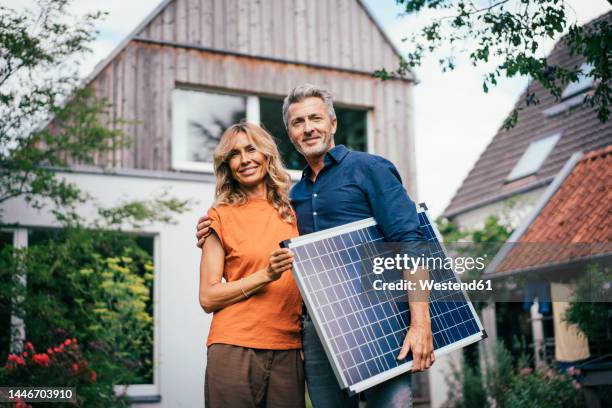 smiling mature couple standing with solar panel in front of house - best ager paar garten stock-fotos und bilder