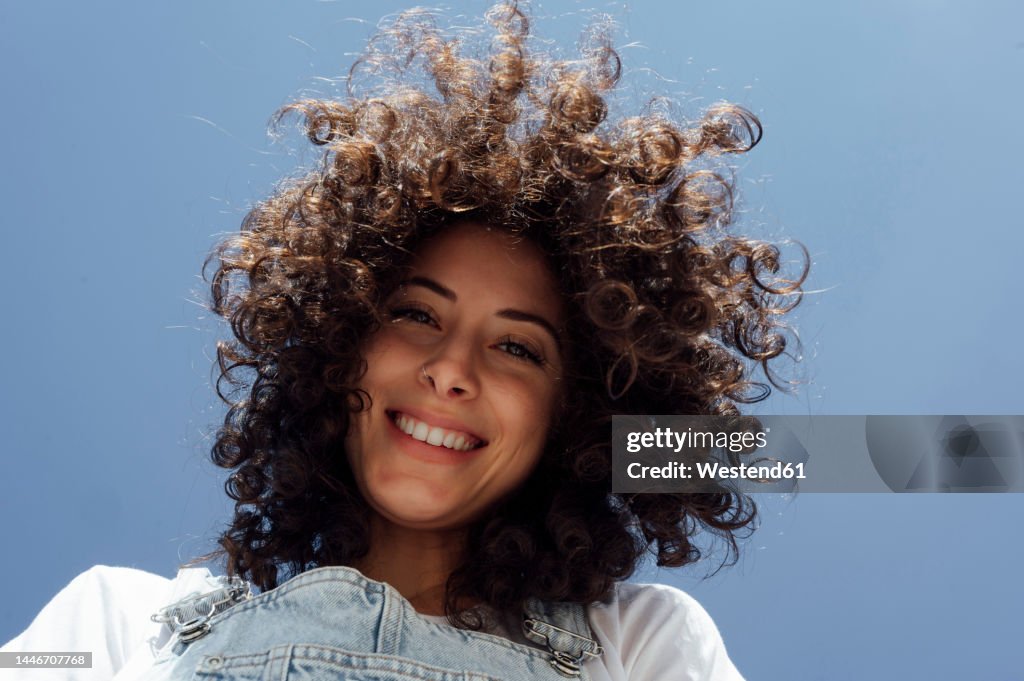 Happy beautiful woman with curly hair under blue sky