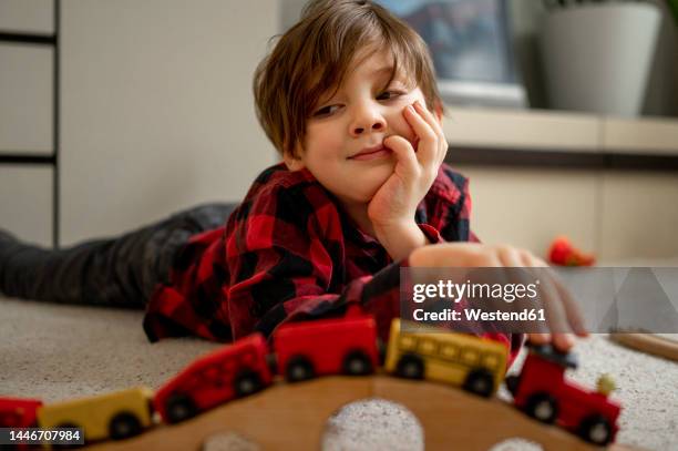 cute boy playing with wooden toy train lying on floor at home - modelleisenbahn stock-fotos und bilder