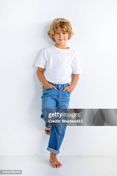 cute boy with hands in pockets leaning on white background - 8 9 anos imagens e fotografias de stock