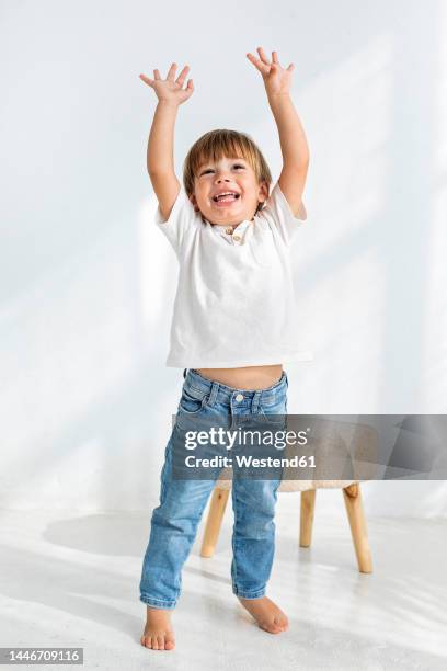 boy with arms raised standing in front of wall at home - physical stance stock pictures, royalty-free photos & images