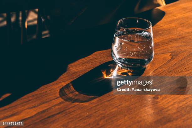 a glass of sparkling water standing on a sunlit wooden table casting shadows and lensflare - sparkling water glass stock-fotos und bilder