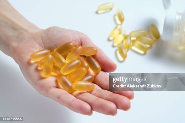 a woman holds omega-3 fish oil capsules in the palm of her hand or in her hand. healthy lifestyle, prevention and treatment of diseases. the girl takes and drinks dietary supplements and vitamins. biologically active additive. intake of healthy fats. - fish oil stock photos et images de collection