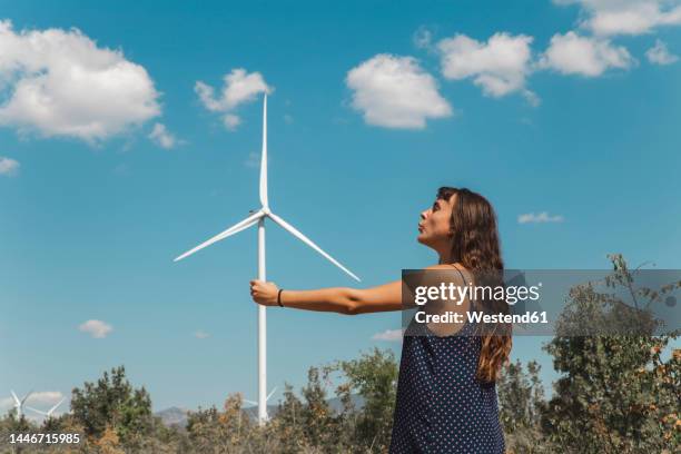 young woman standing in front of wind turbine - optische illusion stock-fotos und bilder