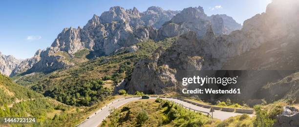 spain, castile and leon, posada de valdeon, panoramic view of picos de europa range in summer with asphalt road in foreground - picos de europa fotografías e imágenes de stock