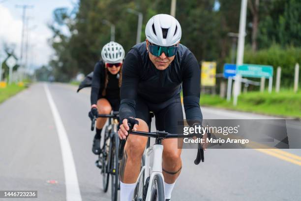 couple are on their white bicycles that drive through the roads of cajica-cundinamarca wearing their safety helmets and cycling glasses - camisola de ciclismo imagens e fotografias de stock