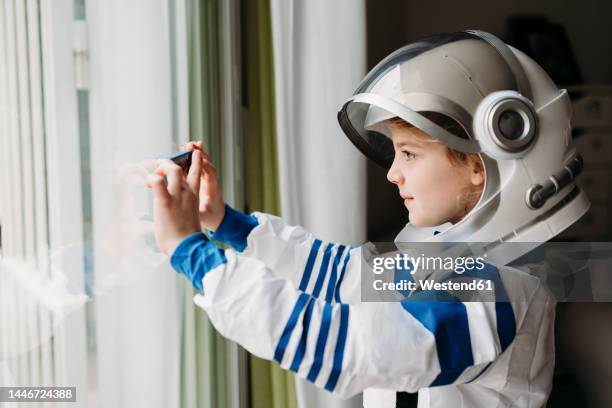 girl wearing space costume photographing through mobile phone at home - astronaut helmet stock pictures, royalty-free photos & images