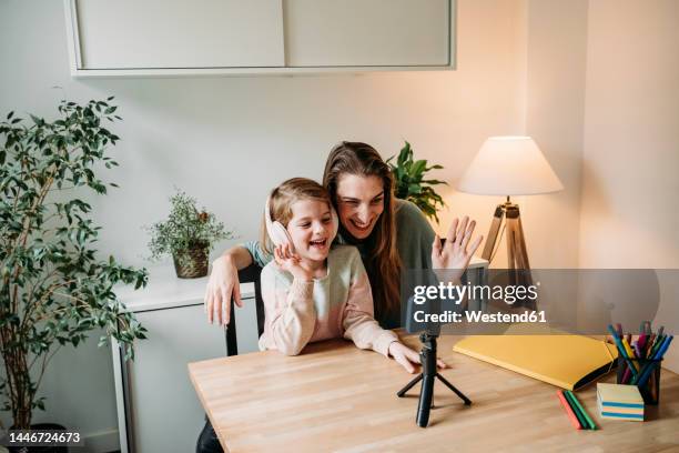 happy daughter with mother having video call on mobile phone at home - tripod stock-fotos und bilder