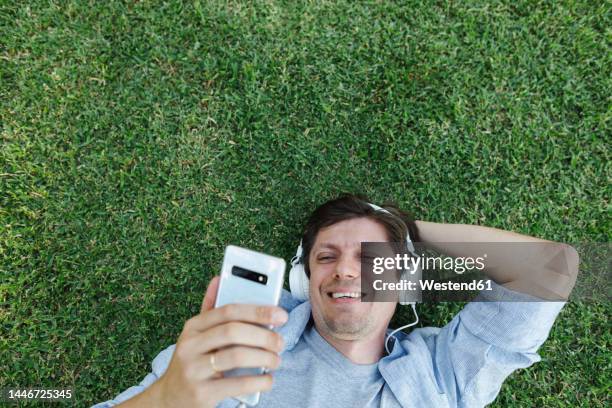 happy man wearing headphones and using smart phone in grass - homens de idade mediana imagens e fotografias de stock