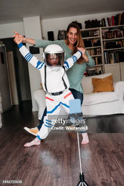 daughter wearing space costume dancing with mother and recording on mobile phone at home - child facebook stockfoto's en -beelden