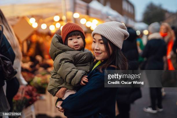 young asian mother shopping with toddler daughter at christmas market - real people shopping stock pictures, royalty-free photos & images