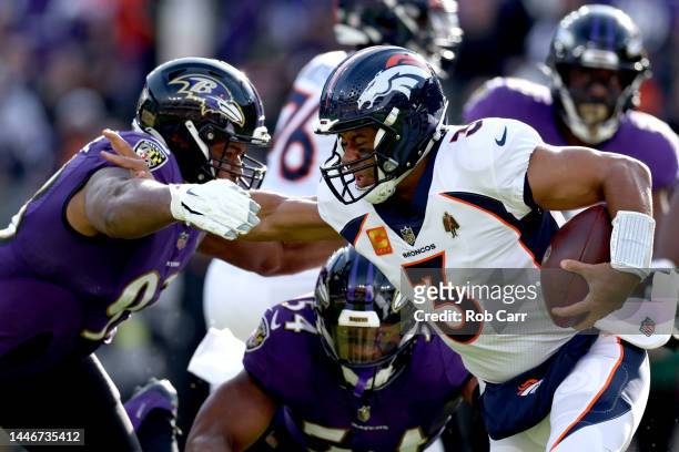Russell Wilson of the Denver Broncos stiff arms Calais Campbell of the Baltimore Ravens on a run in the first quarter at M&T Bank Stadium on December...