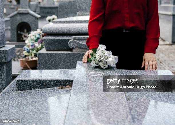 woman in red blouse putting flowers to a loved one in the cemetery. - death stock-fotos und bilder