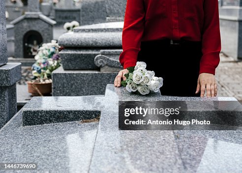 Woman in red blouse putting flowers to a loved one in the cemetery.