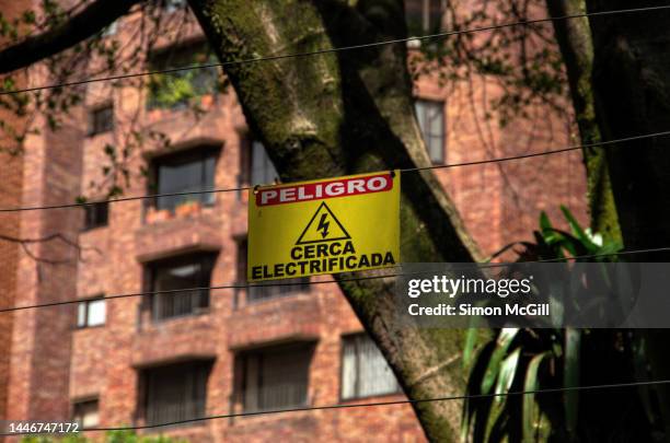 spanish-language warning sign stating 'peligro. cerca electrificada' [danger. electrified fence] on an electric fence surrounding an apartment building complex - peligro stock pictures, royalty-free photos & images