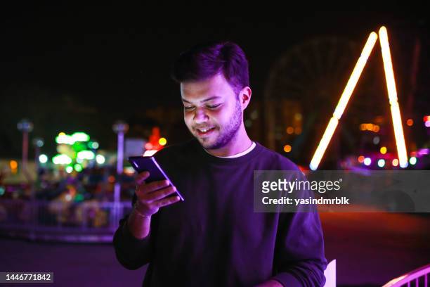 glücklicher junger mann spielt spiele auf seinem handy mit bunten lichtern bokeh im hintergrund - asian games day 1 stock-fotos und bilder