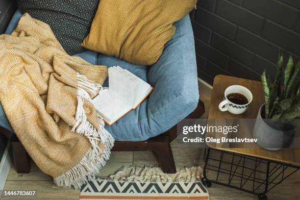 cozy decorated place for relaxation on balcony. armchair with pillows and plaid, coffee table, opened book - nicho imagens e fotografias de stock