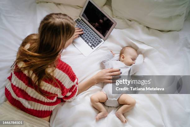 freelance remote work for young mothers. directly above. young woman work and study with laptop, lying with little baby on bed - maternity leave stockfoto's en -beelden