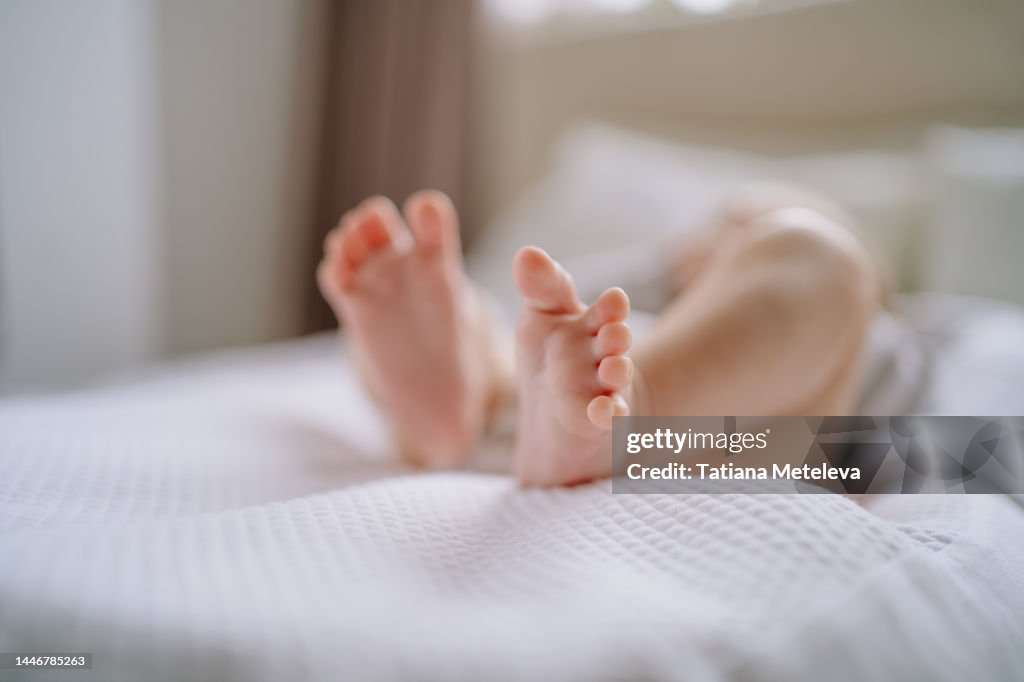 Cute small bare feet of newborn baby, lying in white linen