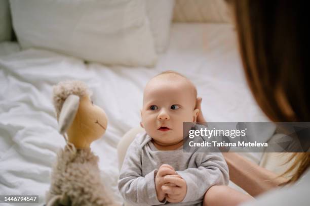 little curious and surprised baby looking at ship toy and play with mother in bed - bébé doudou photos et images de collection