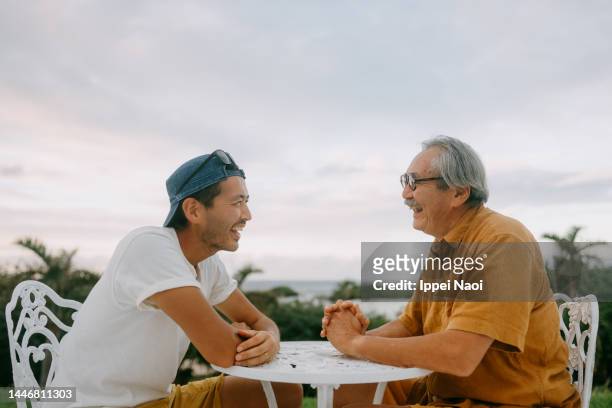 senior father and adult son chatting on patio - asian man sitting at desk stock pictures, royalty-free photos & images